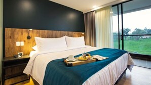 A modern hotel room with a large bed, a wooden headboard, a bedside table with a lamp, and a tray with breakfast items. - Hotel Lagoon (Rionegro)