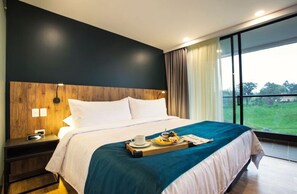 A modern hotel room with a large bed, a wooden headboard, a bedside table with a lamp, and a tray with breakfast items. - Hotel Lagoon (Rionegro)