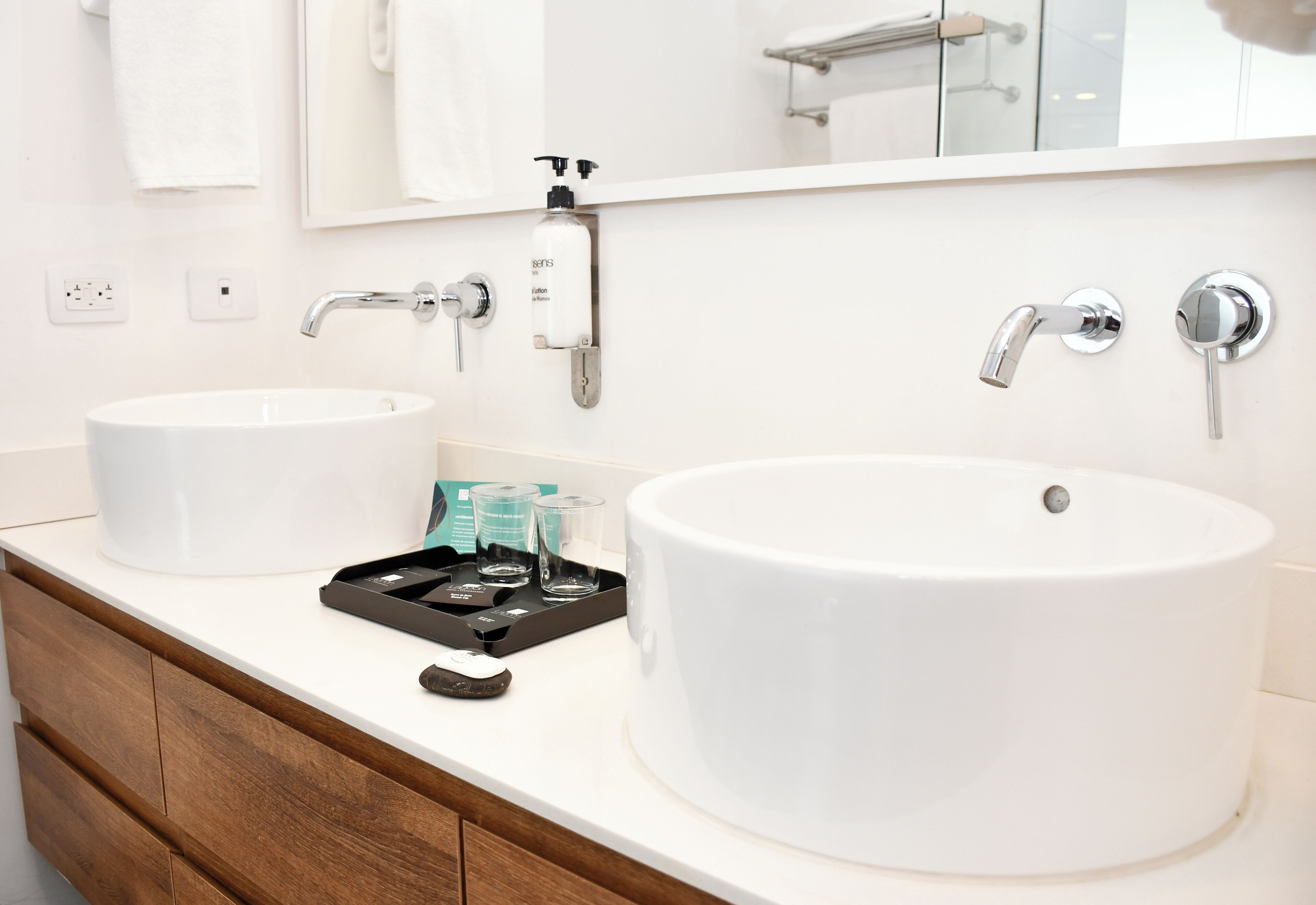 A bathroom with two sinks, a mirror, a soap dispenser, and a tray with toiletries.