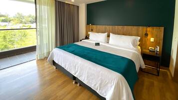A hotel room with a large bed, wooden headboard, and a view of greenery outside.