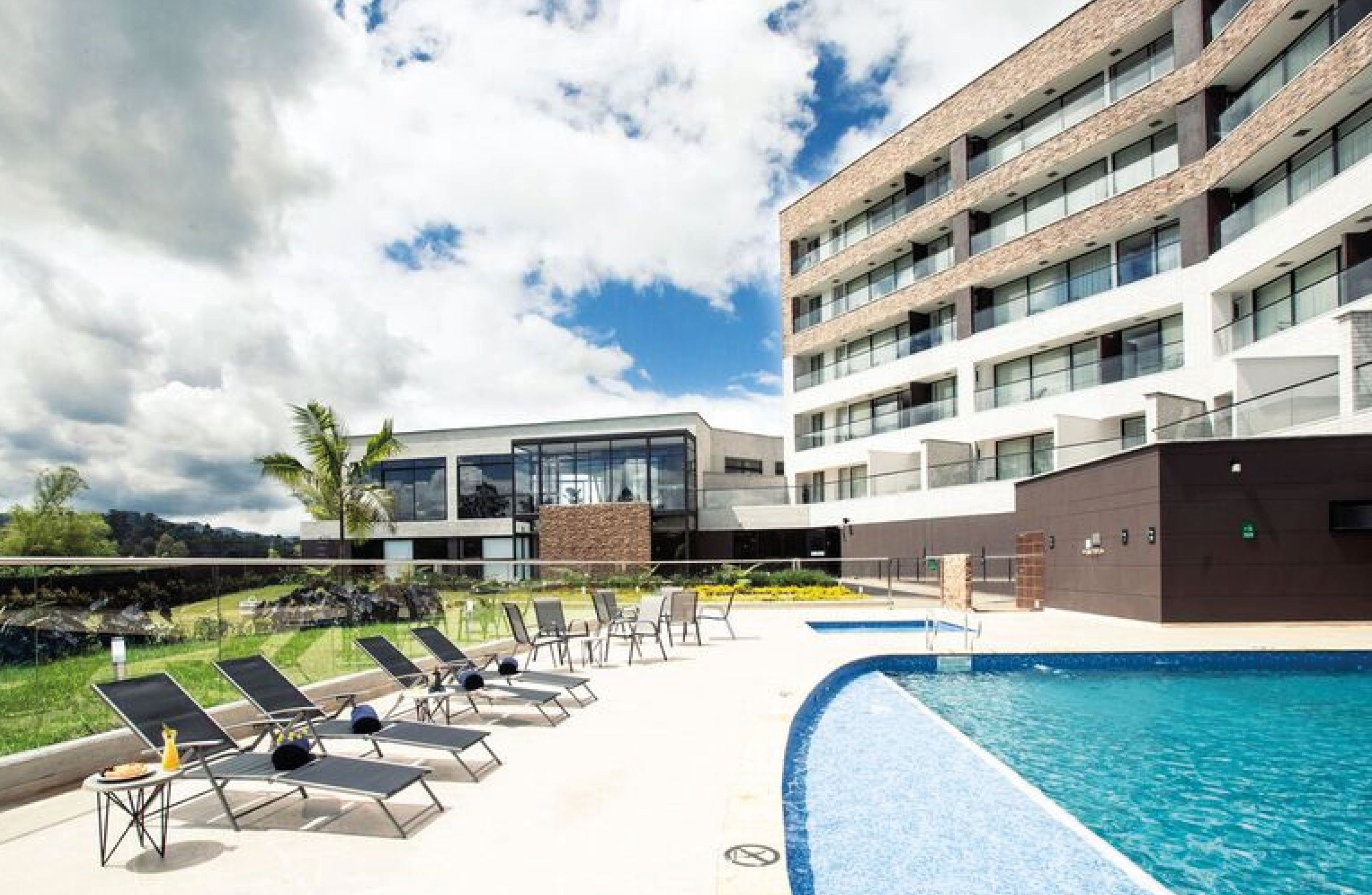A modern hotel with a swimming pool, lounge chairs, and a view of the surrounding landscape.