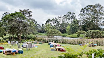 Un área de estar al aire libre con mesas y sillas, rodeada de abundante vegetación y un lago.
