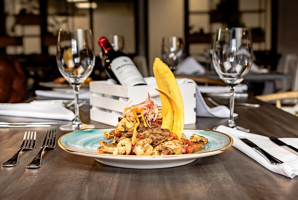 Un plato de mariscos con un detalle decorativo sobre una mesa de madera, acompañado de copas de vino y una botella.