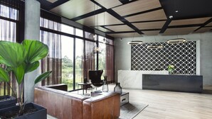 A modern reception area with a wooden reception desk, large potted plants, and a view of the outdoors through large windows. - Hotel Lagoon (Rionegro)