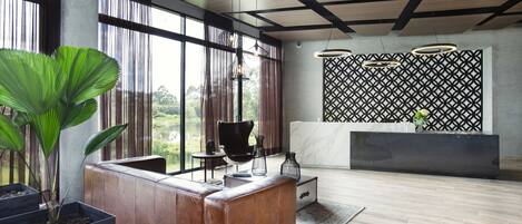 A modern reception area with a wooden reception desk, large potted plants, and a view of the outdoors through large windows.