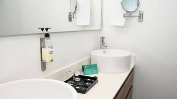 A modern bathroom with a large white sink, a mirror, a towel rack, a soap dispenser, and a tray with toiletries.