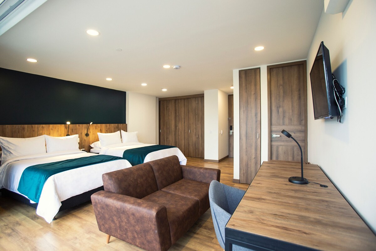A hotel room with two beds, a desk, a chair, and a TV mounted on the wall.