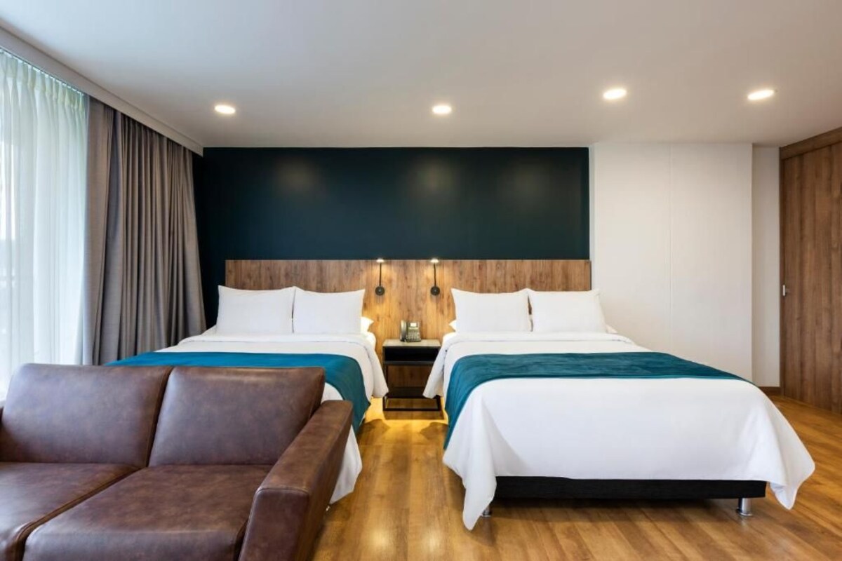 A hotel room with two beds, a sofa, and a wooden floor.