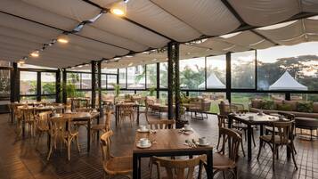 A spacious outdoor dining area with tables and chairs, large windows, and a view of the surrounding landscape.