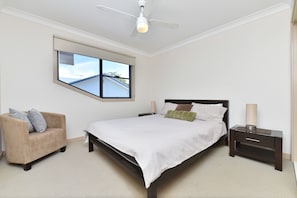 A bedroom with a bed, a chair, a nightstand, a lamp, and a ceiling fan.