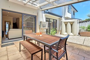 Een terras buiten met een tafel, stoelen, een plafondventilator en een schuifdeur die leidt naar de binnenruimte.