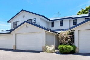 Een huis met twee verdiepingen, een garage, een kleine tuin en een helderblauwe lucht.