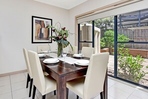 Een eethoek met een tafel voor vier personen, stoelen, een vaas met bloemen en een lijst met een afbeelding aan de muur.