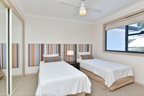 Een hotelkamer met twee bedden, een plafondventilator, een raam met uitzicht en een gestreept hoofdeinde.
