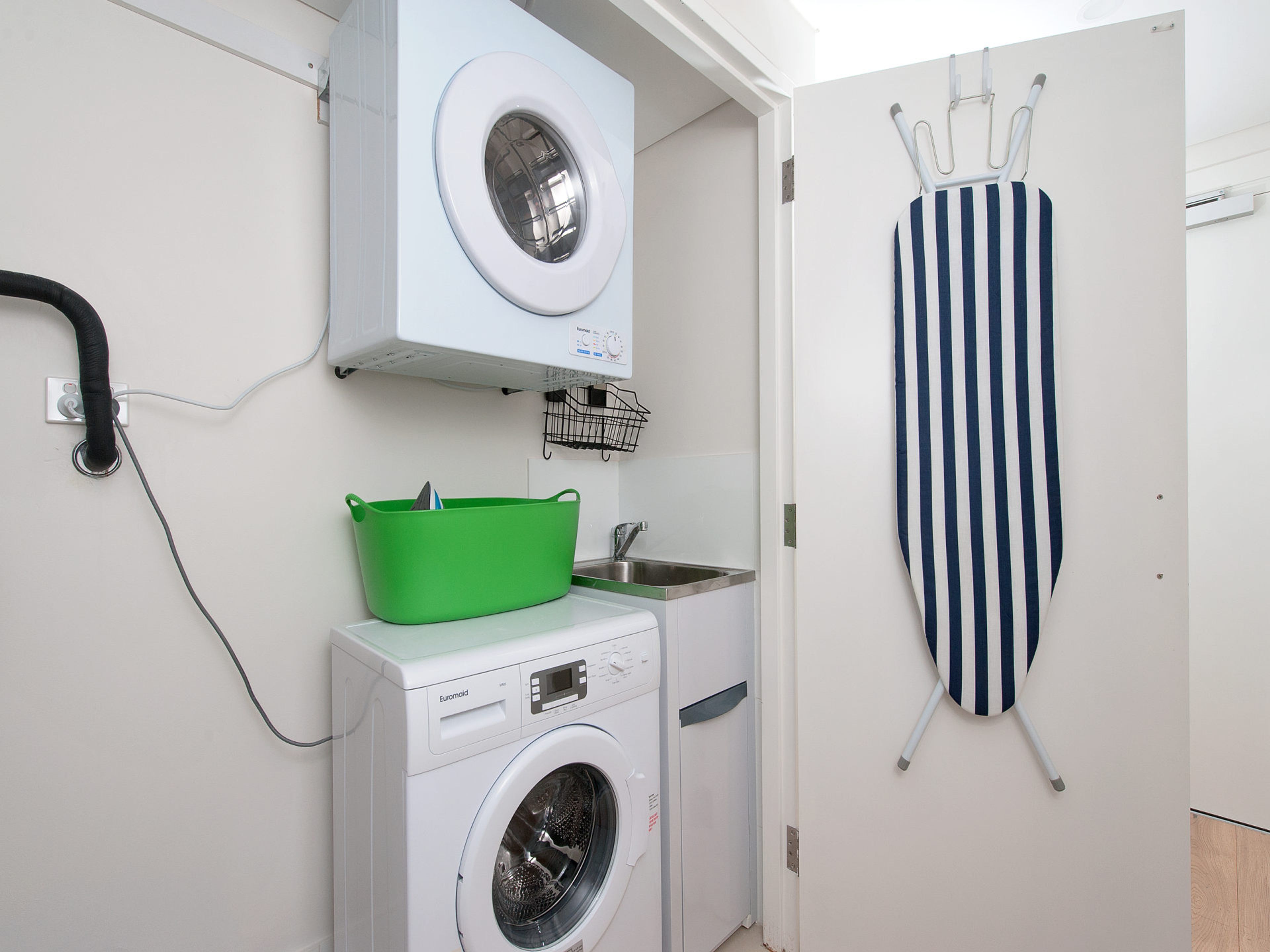 A laundry area with a washing machine, a drying rack, and a green basket.
