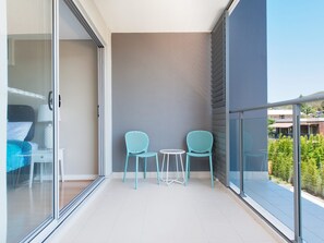 Ein Balkon mit zwei Stühlen und einem kleinen Tisch, eine Schiebetür zum Schlafzimmer und Blick auf eine Wohngegend.