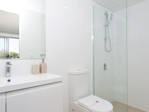 Een moderne badkamer met een glazen douchecabine, een wit wastafeltje en een toilet.