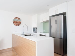 Una cocina moderna con armarios blancos, un refrigerador de acero inoxidable y piso de madera.
