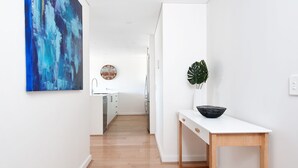 Eine moderne Küche mit weißen Schränken, Holzboden, einer Uhr und einer Pflanze auf einem weißen Tisch.