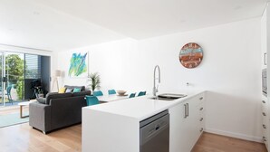 Eine moderne Küche mit einer zentralen Kochinsel, einem Essbereich mit Sofa und Stühlen sowie einem großen Fenster mit Blick ins Freie.