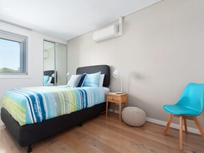Un dormitorio moderno con cama, lámparas de noche, una silla y un otoman redondos.
