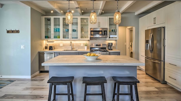 A modern kitchen with white cabinetry, a central island, bar stools, and pendant lighting. - Remodeled Ventura Beach Home with Yard & Fire Pit! (Ventura)