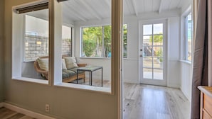 A room with a large window, a wicker chair, and a small table. - Remodeled Ventura Beach Home with Yard & Fire Pit! (Ventura)