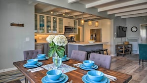 A dining area with a wooden table set for six, blue bowls, and a vase with flowers. - Remodeled Ventura Beach Home with Yard & Fire Pit! (Ventura)