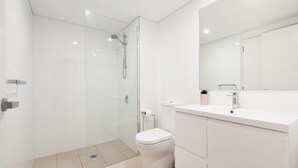 Et moderne badeværelse med brusekabine i glas, et hvidt toilet og en vask med spejl.