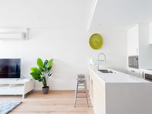 Une cuisine moderne avec un plan de travail blanc, des appareils en acier inoxydable et une horloge verte au mur.