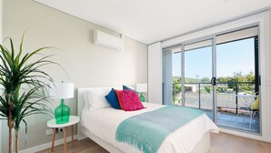 Et moderne soveværelse med en stor seng, en grøn vase, et lille bord og udsigt til en balkon.
