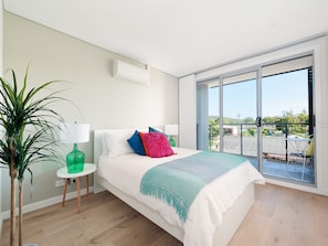 Een moderne slaapkamer met een groot bed, een groene vaas, een klein tafeltje en uitzicht op een balkon.