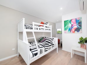Un lit superposé avec une échelle, une petite table et un tableau abstrait aux couleurs vives accroché au mur.
