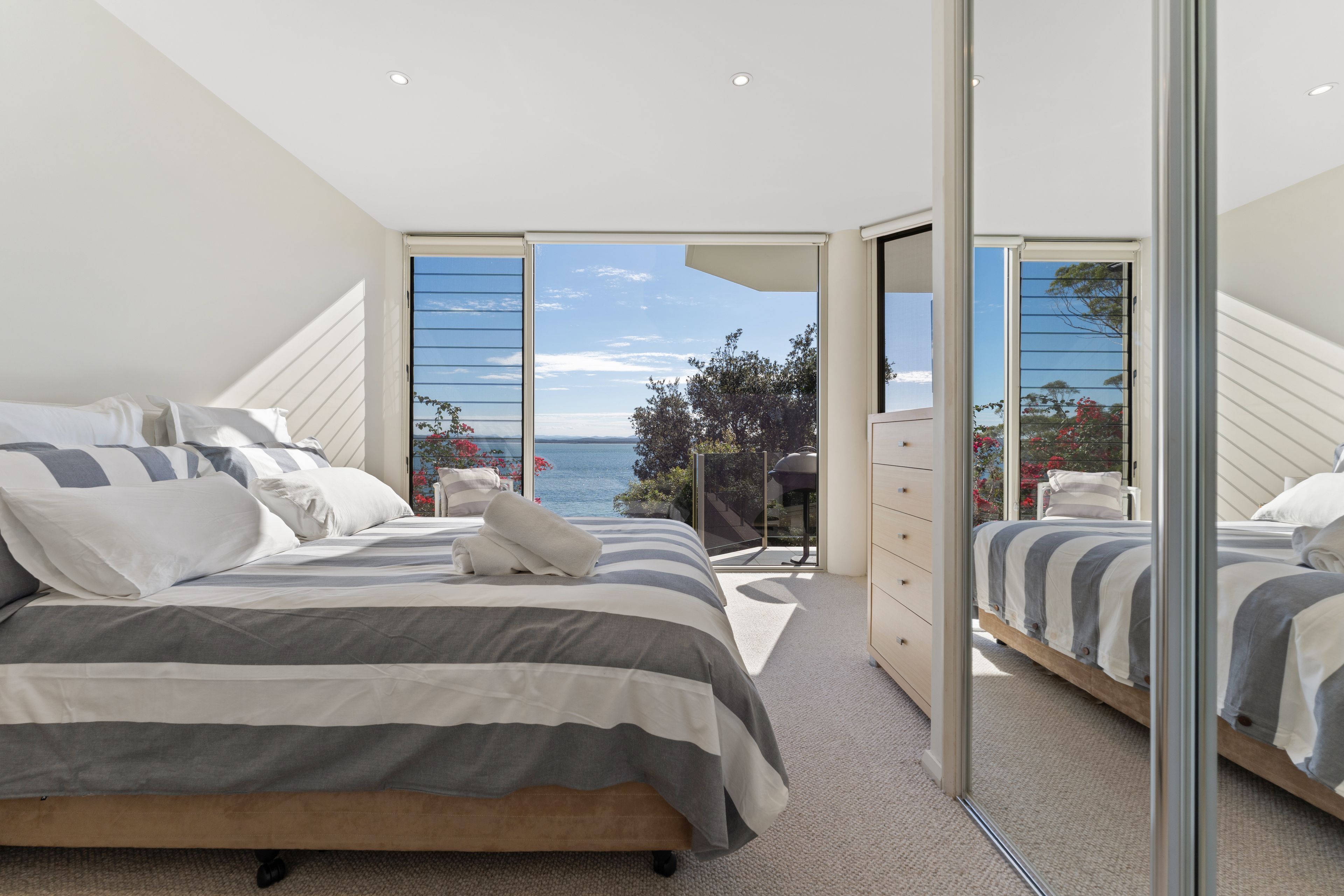 A bedroom with a large bed, a dresser, and a view of the sea through a glass door.