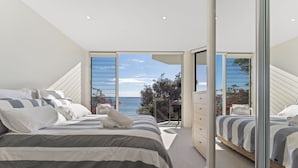 A bedroom with a large bed, a dresser, and a view of the sea through a glass door. - Mirage Holiday Home with Water Views Nelson Bay (Nelson Bay)