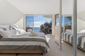 Een slaapkamer met een groot bed, een kaptafel en uitzicht op zee door een glazen deur.