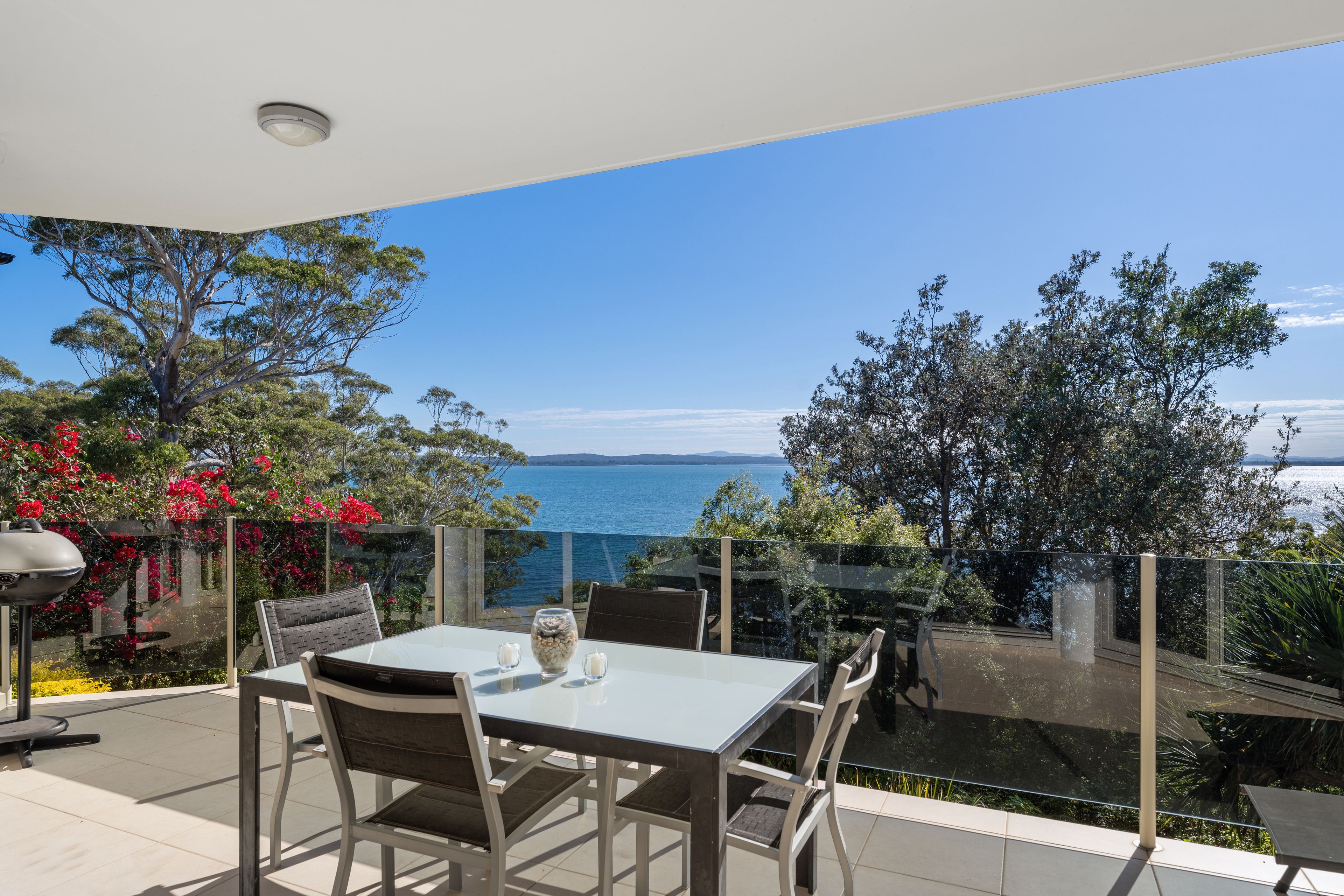 An outdoor dining area with a table and chairs, overlooking a body of water and a mountainous landscape.