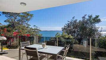 An outdoor dining area with a table and chairs, overlooking a body of water and a mountainous landscape.