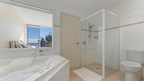 A bathroom with a bathtub, a glass-enclosed shower, and a toilet. - Mirage Holiday Home with Water Views Nelson Bay (Nelson Bay)