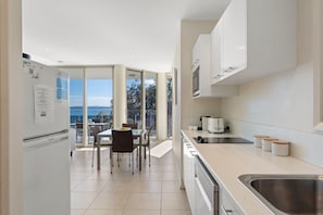 A modern kitchen with a dining area, large windows, and a view of the sea.