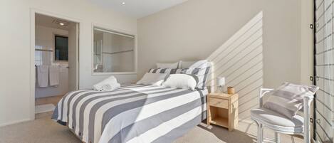 Une chambre à coucher comprenant un lit, une table de chevet, une chaise, un miroir et donnant sur une salle de bain.
