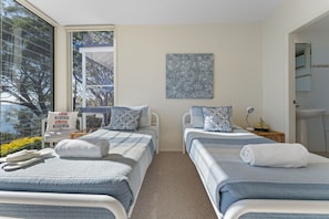 Een hotelkamer met twee bedden, een groot raam met uitzicht op bomen, een schilderij aan de muur en een badkamer die door een geopende deur zichtbaar is.