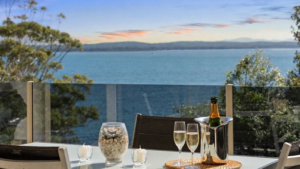 Une table avec une bouteille de champagne, deux verres et un bol décoratif rempli de petits galets.