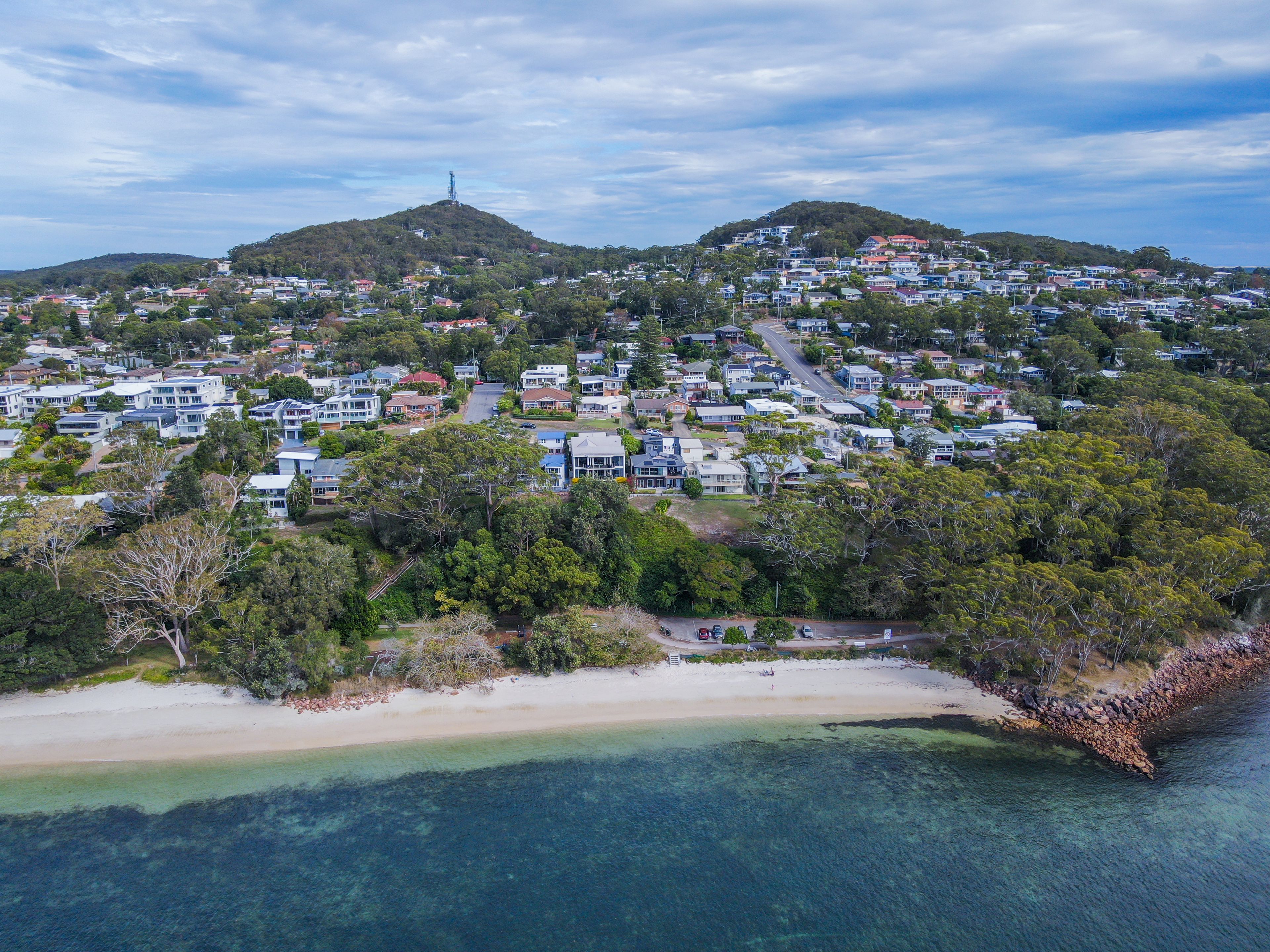 A coastal residential area with houses, a beach, and hills in the background.
