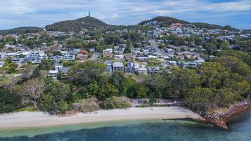 A coastal residential area with houses, a beach, and hills in the background.