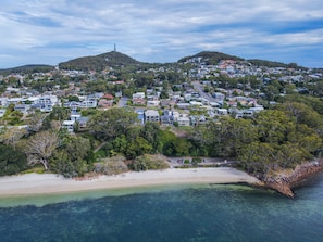 A coastal residential area with houses, a beach, and hills in the background.