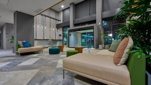 A modern lounge area with a sofa, ottoman, and hanging lights. - City Express Plus by Marriott Tampico (Tampico)