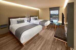 A hotel room with two beds, a desk, a chair, and a TV.