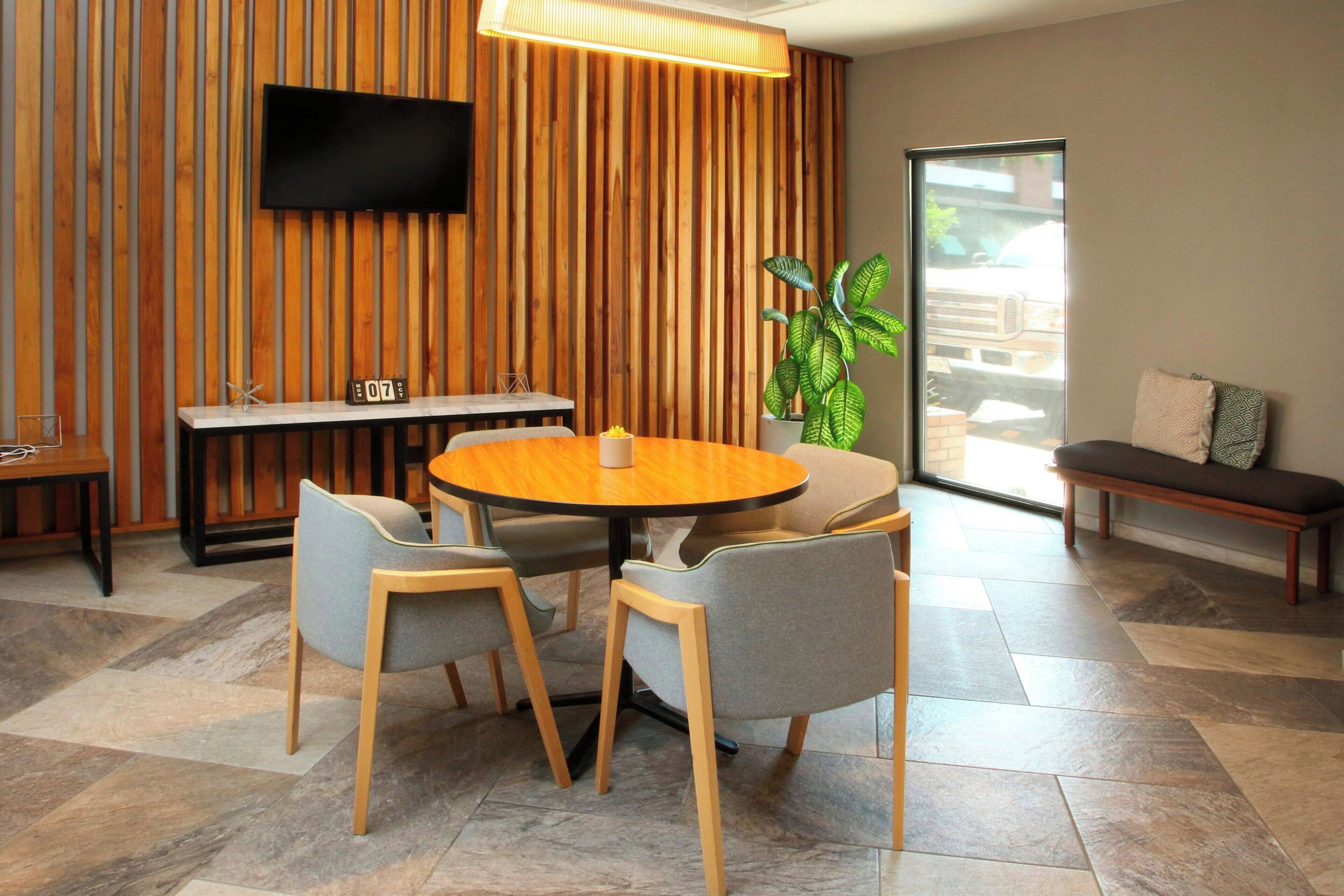 A modern dining area with a round table, four chairs, a TV mounted on a wooden wall, and a bench with cushions.