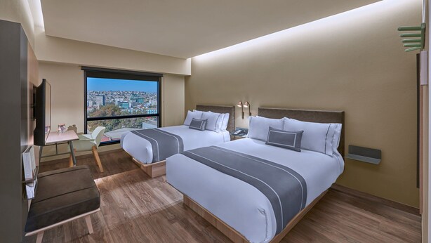 A hotel room with two beds, a desk, a chair, a TV, and a large window offering a city view. - City Express Plus by Marriott Tampico (Tampico)